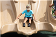 boy in blue shirt reaches bottom of slide