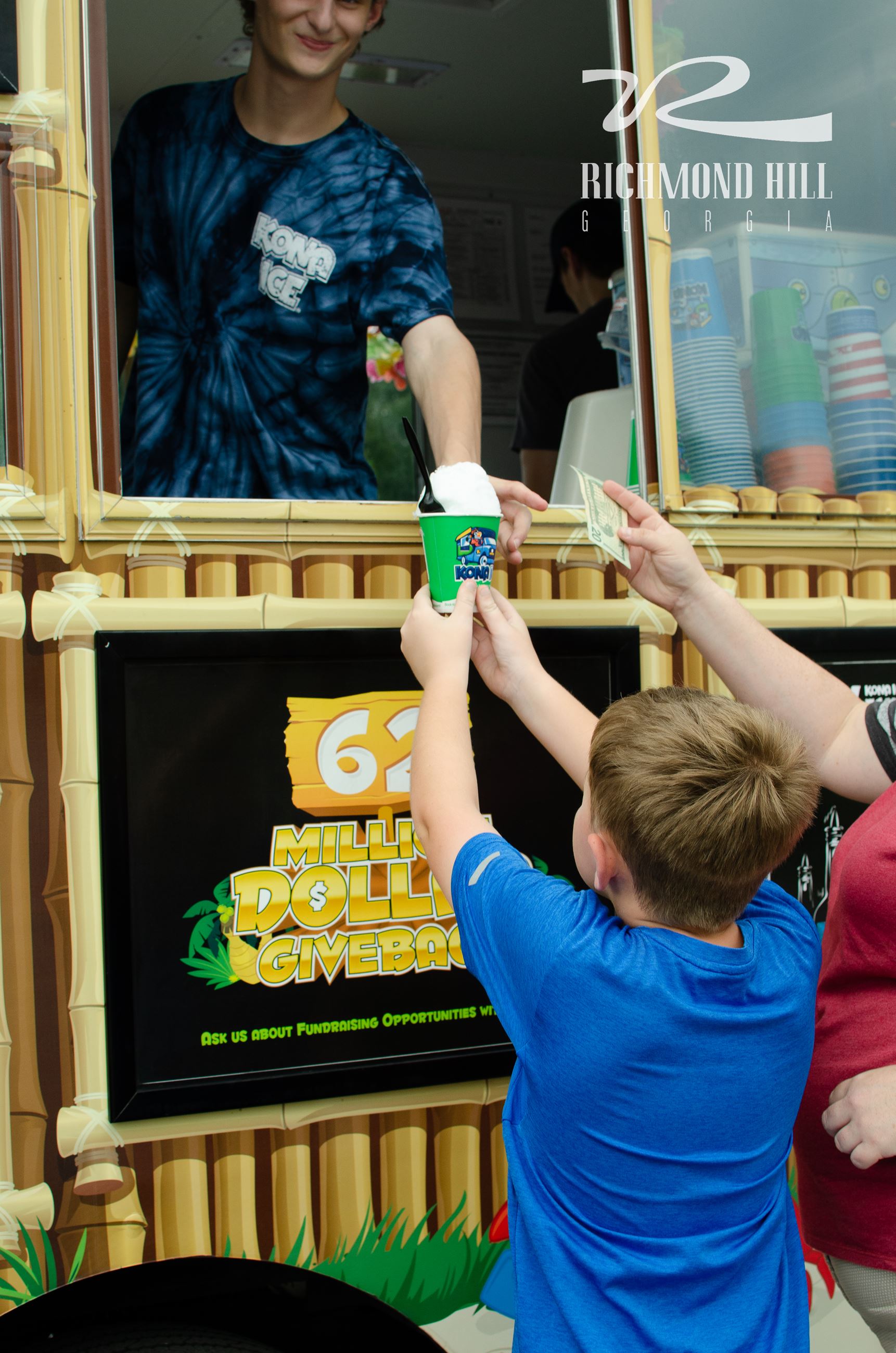 a vendor hands a corndog to a boy wearing a blue shirt